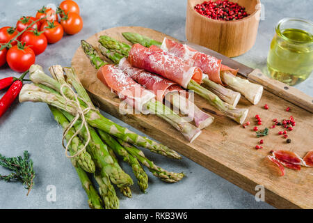 Frische organische Spargel in Schinken auf einem Schneidebrett gewickelt. Stockfoto