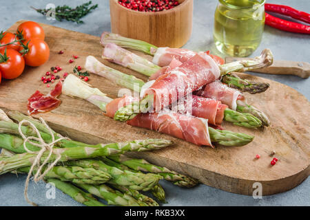 Frische organische Spargel in Schinken auf einem Schneidebrett gewickelt. Stockfoto