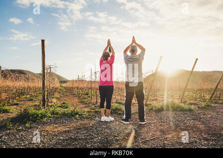 Ständigen Yoga Übung mit alten senior Paar mit Blick auf den Sonnenuntergang Sport Fitness gesund zu bleiben - Natur und Outdoor Genuss lifest Stockfoto