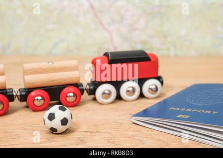 Red Spielzeugeisenbahn und Fußball in der Nähe von einen biometrischen Pass liegen auf einem alten Holztisch gegen eine Karte Stockfoto