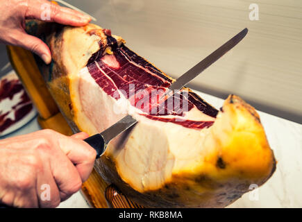 Blick auf eine Hand und Messer schneiden Spanischen Schinken Stockfoto