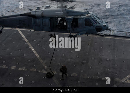Marines mit 31 Marine Expeditionary Unit's Force Reconnaissance Platoon schnelle Seil von einem MH-60S Sea Hawk bei einem Besuch, Board, Durchsuchung und Beschlagnahme Übung an Bord der USNS Charles Drew (T-AKE 10), Philippine Sea, Feb 6, 2019. Während des simulierten VBSS, Marines mit FRP probten die Beschlagnahme und Sicherstellung einer simulierten feindlichen Schiff mit Geschwindigkeit und entscheidende Maßnahmen Kontrolle der Brücke des Schiffes, den Maschinenraum und Viertel zu gewinnen. Die 31. MEU, das Marine Corps' nur kontinuierlich vorwärts - bereitgestellt MEU partnering mit dem Wasp amphibischen bereit, Gruppe, bietet eine flexible und tödlicher Gewalt bereit zu perfo Stockfoto