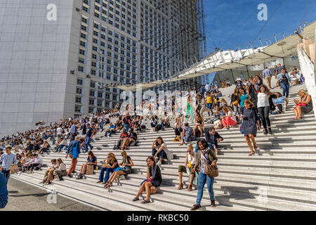 Massen von Menschen sitzen auf den Stufen des La Grande Arche de la Défense genießen Sie die warmen Sonnenstrahlen an einem heissen Sommertag in La Défense, Paris, Frankreich Stockfoto