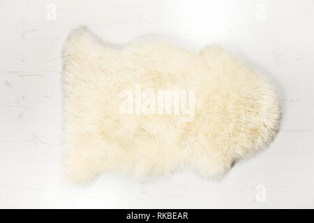 Flach Blick auf die Weißen warme und gemütliche gesamten real dekorative Schaffell Teppich auf weißem Holzbrett Stock. Zimmer für Text. Studio eingestellt. Stockfoto