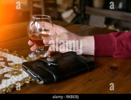 Nahaufnahme eines Mannes auf Halten zu seinem Glas Whiskey on the Rocks und eine Zigarre auf ein elegantes Holz Tisch. Stockfoto