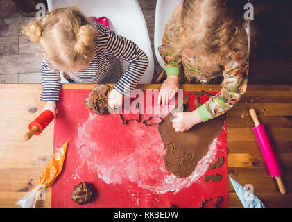 Blick von oben auf die zwei jungen Mädchen Schwestern rolling Plätzchenteig und süßen knackigen Lebkuchen Cookies. Spaß Weihnachten Winter saisonale Aktivitäten. Stockfoto