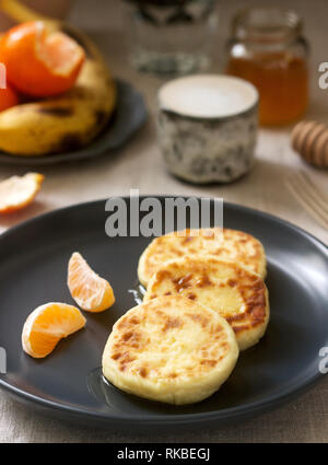 Vegetarisches Frühstück von Quark Pfannkuchen mit Honig, Obst und Kaffee mit Milch. Im rustikalen Stil. Stockfoto