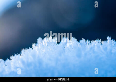 Auf schönen, blauen bokeh Lens Flares Hintergrund, kleine Details der weiß Top von Crystal Schneeflocken von der Sonne Licht erreicht. Stockfoto