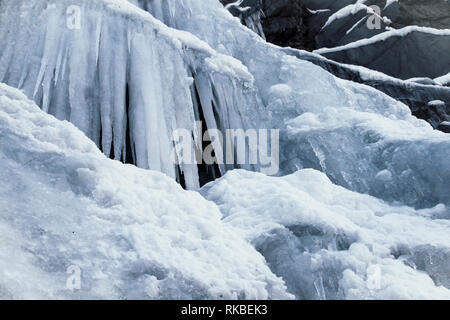 Nahaufnahme, Detail der gefrorenen Wasserfall einschließlich Eis und gefrorenen Stalagtiten, mit Schnee auf den Felsen im Hintergrund auf einem steilen Felsen auf dem Berg. Stockfoto