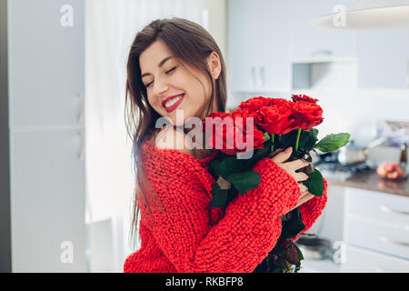 Junge Frau gefunden Blumenstrauß aus Rosen auf Küche. Happy girl Holding und umarmen Blumen. Valentines Tag Stockfoto