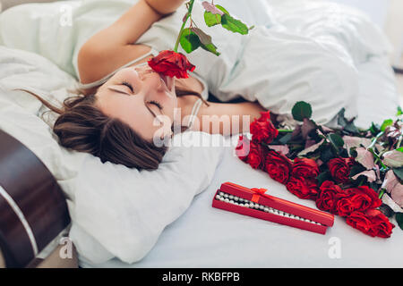 Junge Frau gefunden Blumenstrauß aus Rosen geschmückt mit Schmuck in Geschenkbox im Bett. Happy girl duftende Blumen. Valentines Tag Stockfoto