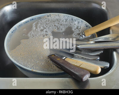 Messer in der Schüssel mit Wasser und Spülmittel in der Küche Spüle gefüllt. Stockfoto