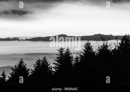 Bäume Silhouetten gegen den Himmel in der Dämmerung, mit Bergen Schichten im Hintergrund Stockfoto