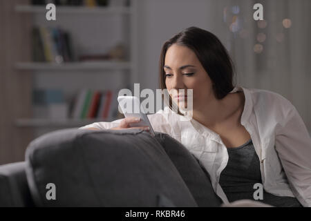 Langeweile Frau Kontrolle smart phone Inhalt sitzen auf einer Couch in der Nacht zu Hause Stockfoto