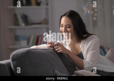 Happy lady Textnachrichten auf Smart Phone auf der Couch zu Hause sitzen in der Nacht Stockfoto