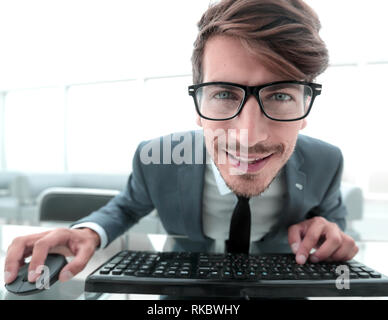Junge Unternehmer mit der Eingabe über die Tastatur des Computers mit lustigen Gesichtsausdruck im Büro isoliert Stockfoto