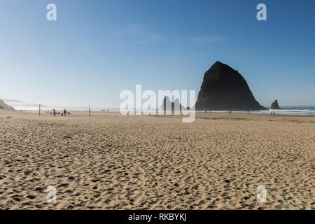Touristen und Einheimische genießen den Strand mit Haystack Rock im Hintergrund bei Cannon Beach, Oregon, USA. Stockfoto