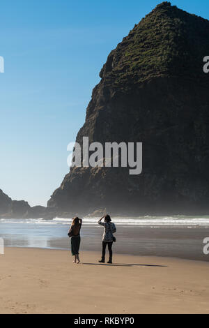 Touristen und Einheimische genießen den Strand mit Haystack Rock im Hintergrund bei Cannon Beach, Oregon, USA. Stockfoto