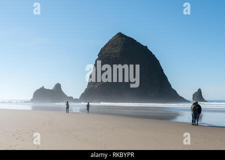 Touristen und Einheimische genießen den Strand mit Haystack Rock im Hintergrund bei Cannon Beach, Oregon, USA. Stockfoto
