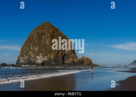 Touristen und Einheimische genießen den Strand mit Haystack Rock im Hintergrund bei Cannon Beach, Oregon, USA. Stockfoto