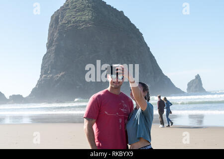 Ein junges Paar von Touristen machen selfies vor dem Haystack Rock in Cannon Beach, Oregon, USA. Stockfoto