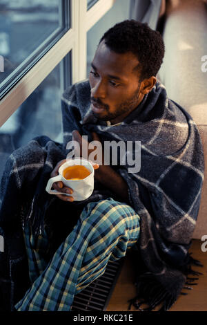 Unternehmer tragen Pyjama in der Nähe der Fenster sitzen, Tee trinken. Stockfoto