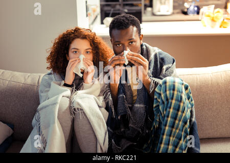 Junges Paar sitzt auf einem Sofa zusammen Leiden vom Niesen Stockfoto