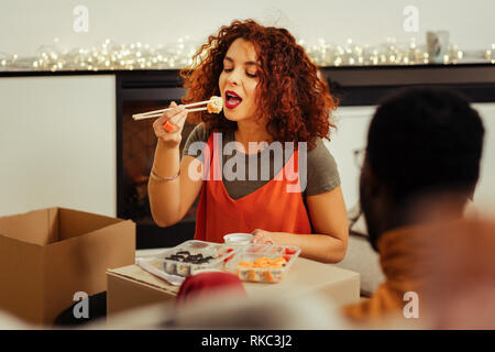 Curly rothaarige Frau Gefühl beim Essen lecker Sushi Roll zufrieden Stockfoto