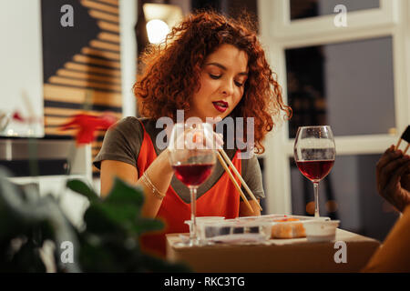 Junge schöne lockige Frau mit hellen Lippen essen Sushi Stockfoto