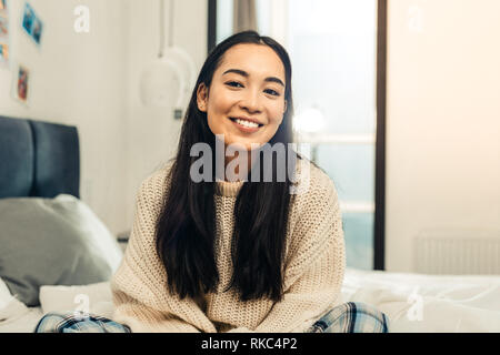 Junge asiatische Frau tragen rosa Pullover sitzt auf ihrem Bett Stockfoto