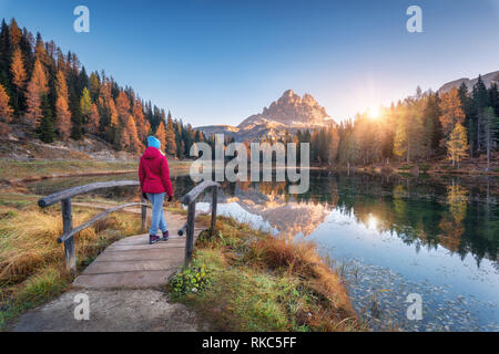 Junge wooman über die kleine Holzbrücke gegen See, Wald, Berg, blauer Himmel mit Sonnenlicht bei Sonnenaufgang. Landschaft mit Mädchen, Reflexion Stockfoto