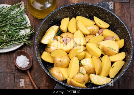 Kartoffelecken mit Meersalz, Rosmarin, Olivenöl auf Skillet. Alte hölzerne Hintergrund Stockfoto