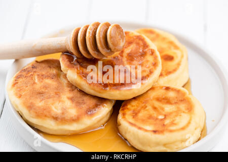 Syrniki, Quark Pfannkuchen mit Honig. Leckeres Frühstück essen. Reich an Calcium Käse Pfannkuchen Stockfoto