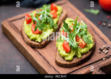 Gesund vegan Toast mit Avocado, Tomaten, Rucola auf Holz, Brett, Detailansicht, Bild horizontal. Snack, Mittagessen oder Veganes Frühstück Stockfoto