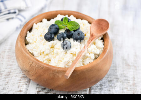 Detailansicht von Hüttenkäse oder Tvorog in Houten auf weißem Holz- Hintergrund. Detailansicht. Hüttenkäse mit Blaubeeren Stockfoto