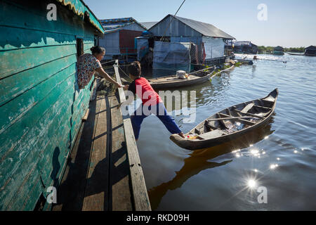 Tonlé Sap See, Kambodscha. Dezember, 2018 19. Junge Guthaben auf seine hölzernen Ruderboot, eine Frau lehnte sich aus dem Fenster in Ihrem schwimmenden hom erreicht. Stockfoto