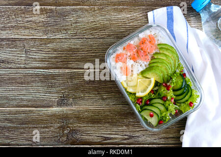 Mittagessen: Reis, Lachs, Salat mit Gurke, Avocado, grünen, Zitrone, Chia Samen und eine Flasche Wasser auf einem hölzernen Hintergrund. Fitness Nahrung. Das Konzept Stockfoto