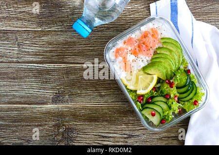 Mittagessen: Reis, Lachs, Salat mit Gurke, Avocado, grünen, Zitrone, Chia Samen und eine Flasche Wasser auf einem hölzernen Hintergrund. Fitness Nahrung. Das Konzept Stockfoto