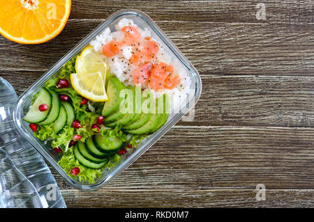 Mittagessen: Reis, Lachs, Salat mit Gurke, Avocado, grünen, Zitrone, Chia Samen und eine Flasche Wasser auf einem hölzernen Hintergrund. Fitness Nahrung. Das Konzept Stockfoto