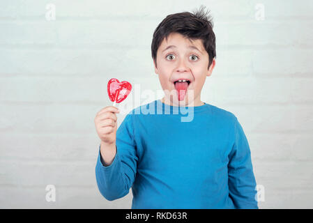 Lustig Kind mit Lollipop heraus haften der Zunge auf den Backstein Hintergrund Stockfoto