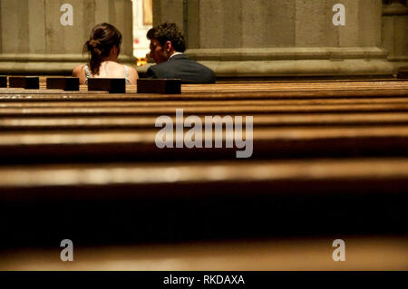 Ein Mann und eine Frau drängten sich und verharrten in einem stillen Gespräch zwischen Kirchenbänken. Stockfoto