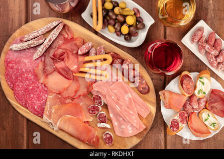 Gourmet Wurstwaren. Eine Auswahl an Wurst und Schinken, Aufschnitt, Schuß von der Oberseite in einem dunklen Holzmöbeln im Landhausstil Hintergrund mit Wein und Oliven Stockfoto