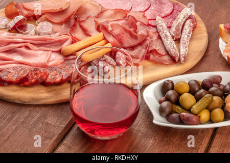 Charcuterie Verkostung. Viele verschiedene Wurst und Schinken, Aufschnitt, auf einem dunklen rustikalen Hintergrund mit einem Glas Rotwein und Oliven Stockfoto
