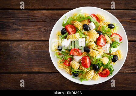 Italienische Pasta Salat mit frischen Tomaten, Käse, Salat und Oliven auf Holz- Hintergrund. Mediterrane Küche. Kochen Mittagessen. Gesunde Ernährung Essen Stockfoto