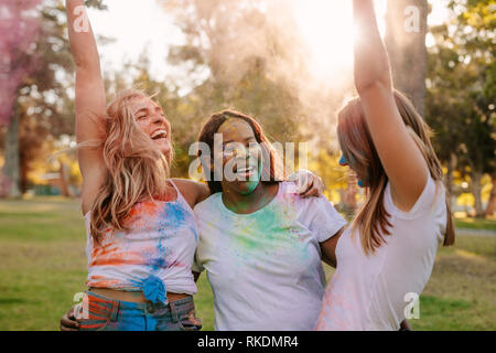 Frauen, die Freunde genießen Holi mit Puder Farben und Tanz in der Freude. Gruppe von drei Frauen, die Freunde holi Spielen in einem Park. Stockfoto