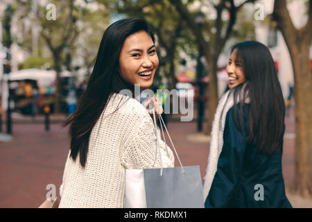 Freundliche asiatische Frau mit einer Einkaufstasche Walking im Freien mit einem Freund. Ansicht der Rückseite zwei asiatische Frauen in der Straße mit einer Einkaufstasche. Stockfoto