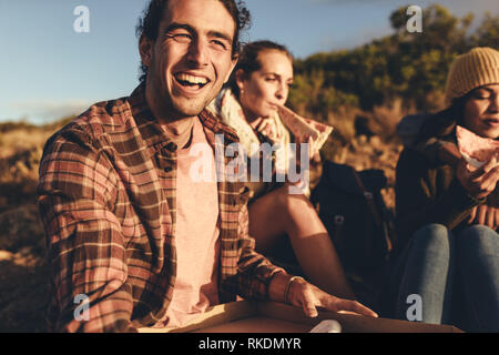 Freunde in Pizza sitzen auf Mountain Trail während Ihrer Wanderung. Gruppe von Mann und Frau auf Wanderung essen Pizza. Stockfoto