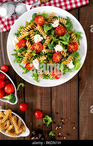 Italienische Pasta Salat mit Vollkorn Fusilli, frische Tomaten, Käse, Salat und Brokkoli auf Holz- rustikalen Hintergrund. Mediterrane Küche. Kochen lu Stockfoto