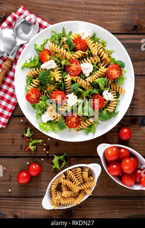 Italienische Pasta Salat mit Vollkorn Fusilli, frische Tomaten, Käse, Salat und Brokkoli auf Holz- rustikalen Hintergrund. Mediterrane Küche. Kochen lu Stockfoto