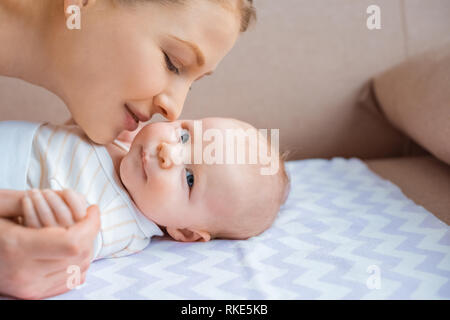 7/8 shot der glücklichen Mutter küssen adorable Kind liegen auf der Couch und Kamera Stockfoto